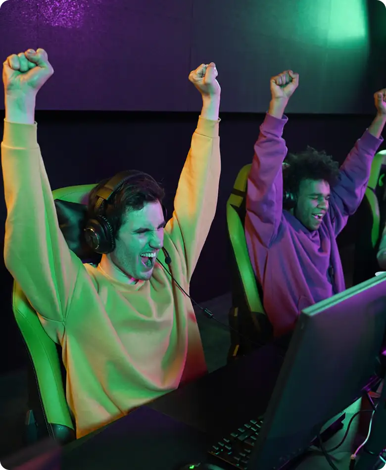 Twee competitieve gamers juichen met opgeheven vuisten na het winnen van een wedstrijd op een gamingcomputer.